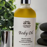 Body oil bottle with a white label on a light background with greenery and stones.