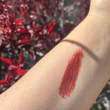 Lipstick swatch on a person's arm with a blurred red floral background