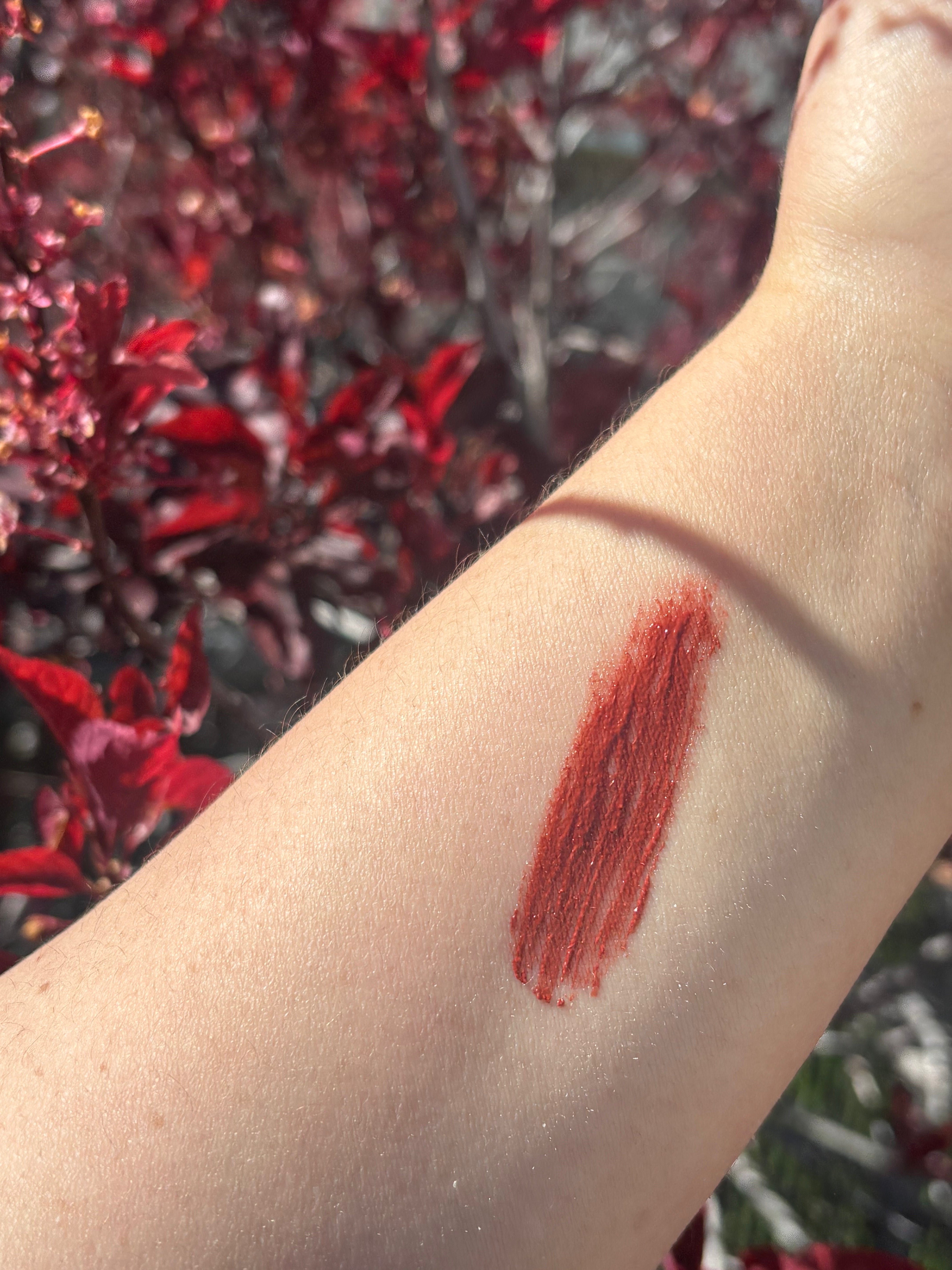 Lipstick swatch on a person's arm with a blurred red floral background