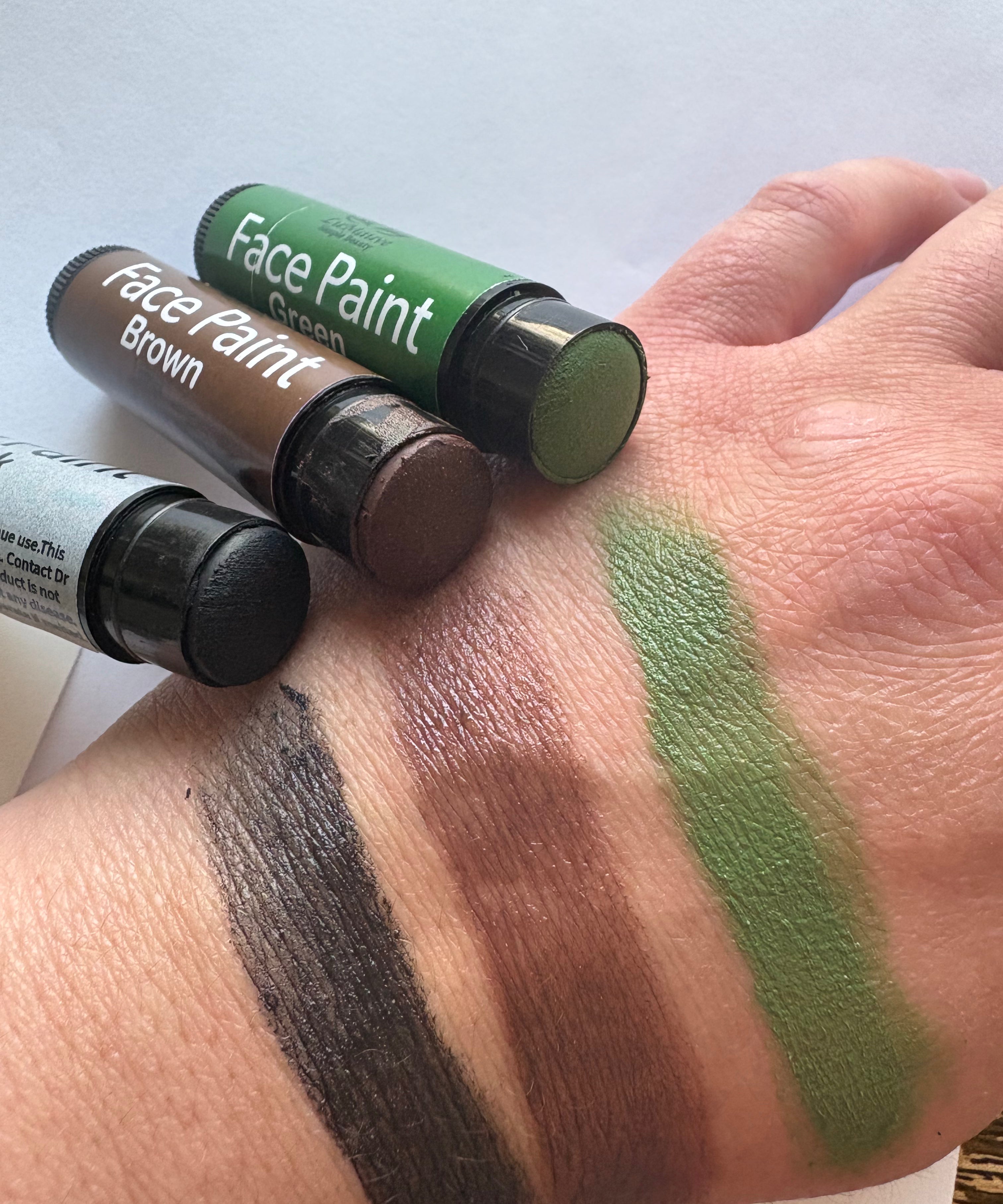 Three face paint tubes with swatches on a wrist