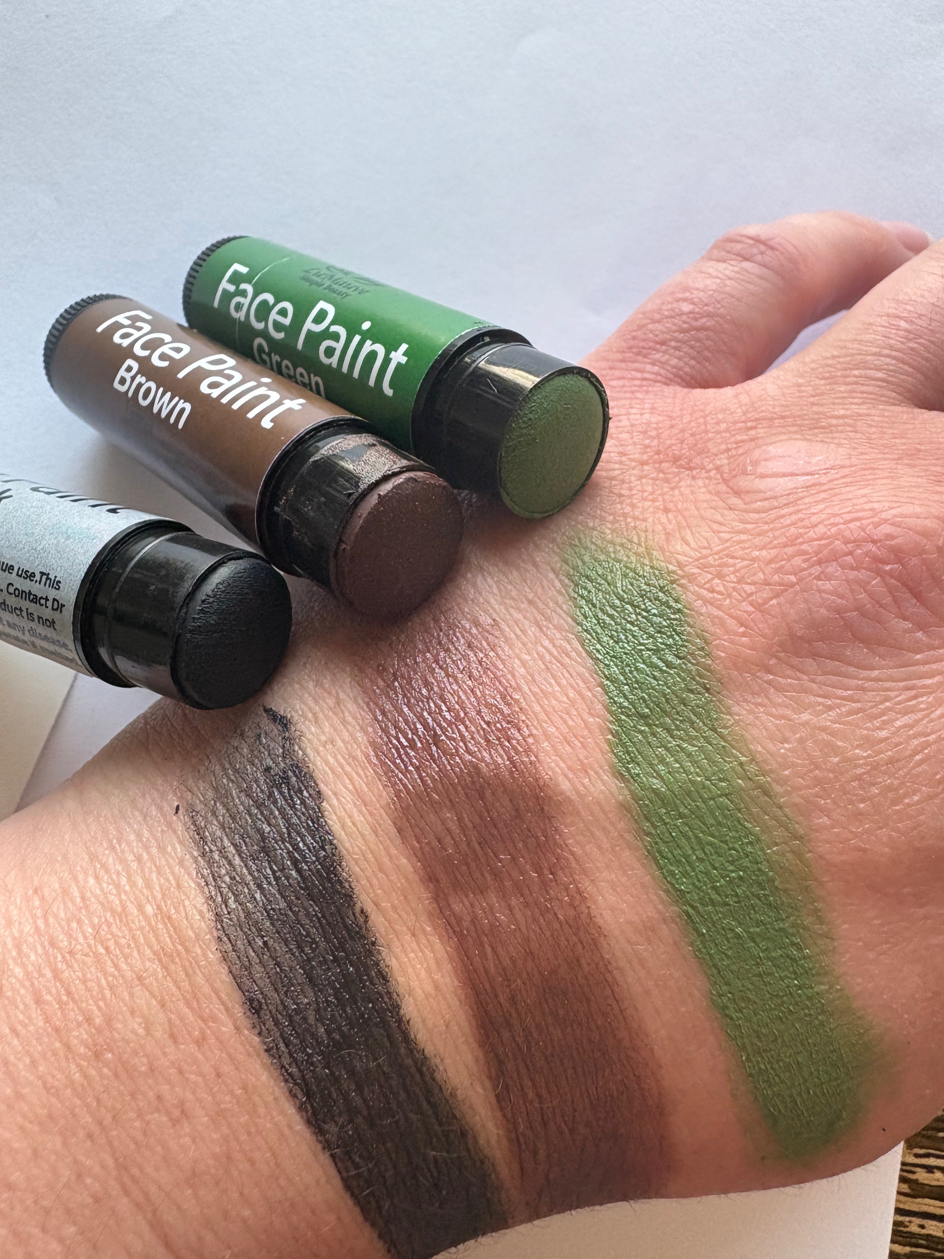 Three face paint tubes with swatches on a wrist