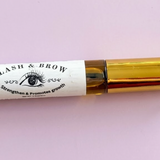 Lash container with gold cap and white label on a light pink background