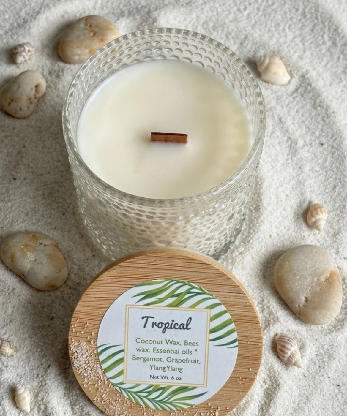 Candle in a glass holder with a wooden lid on a sandy surface with stones

