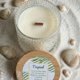 Candle in a glass holder with a wooden lid on a sandy surface with stones


