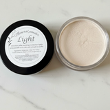 Open container of mineral powder with black lid on a marble surface