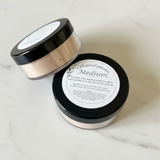 Mineral powder container with black lid and white label on a light background