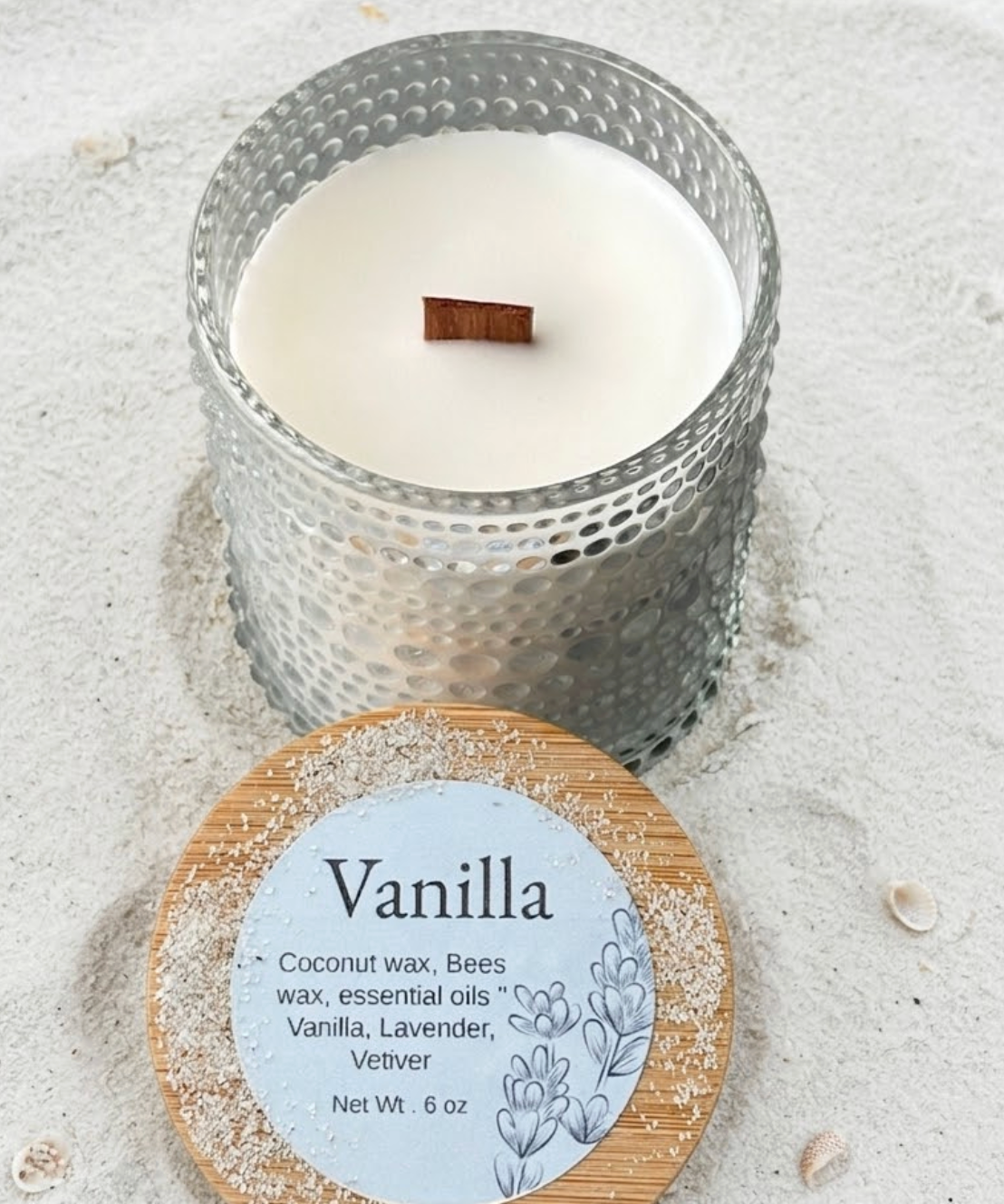 Vanilla-scented candle with wooden wick on sandy surface