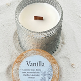 Vanilla-scented candle with wooden wick on sandy surface