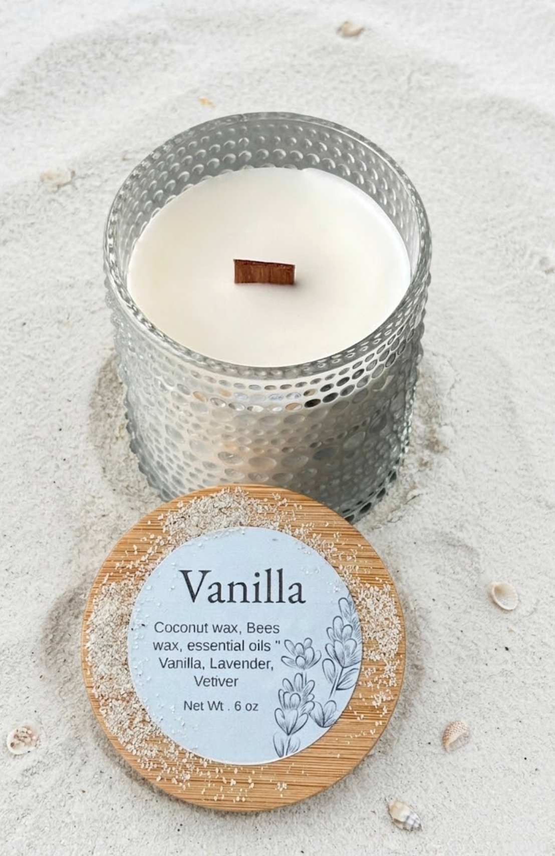 Vanilla-scented candle with wooden wick on sandy surface